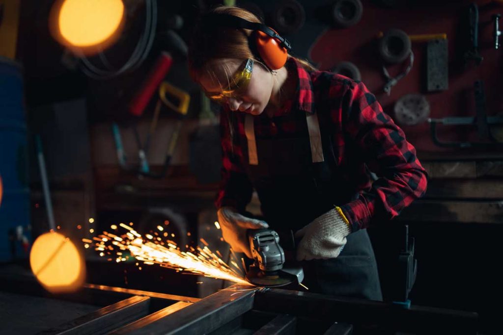 Woman working with angle grinder cuts and polishes metal after welding with spark
